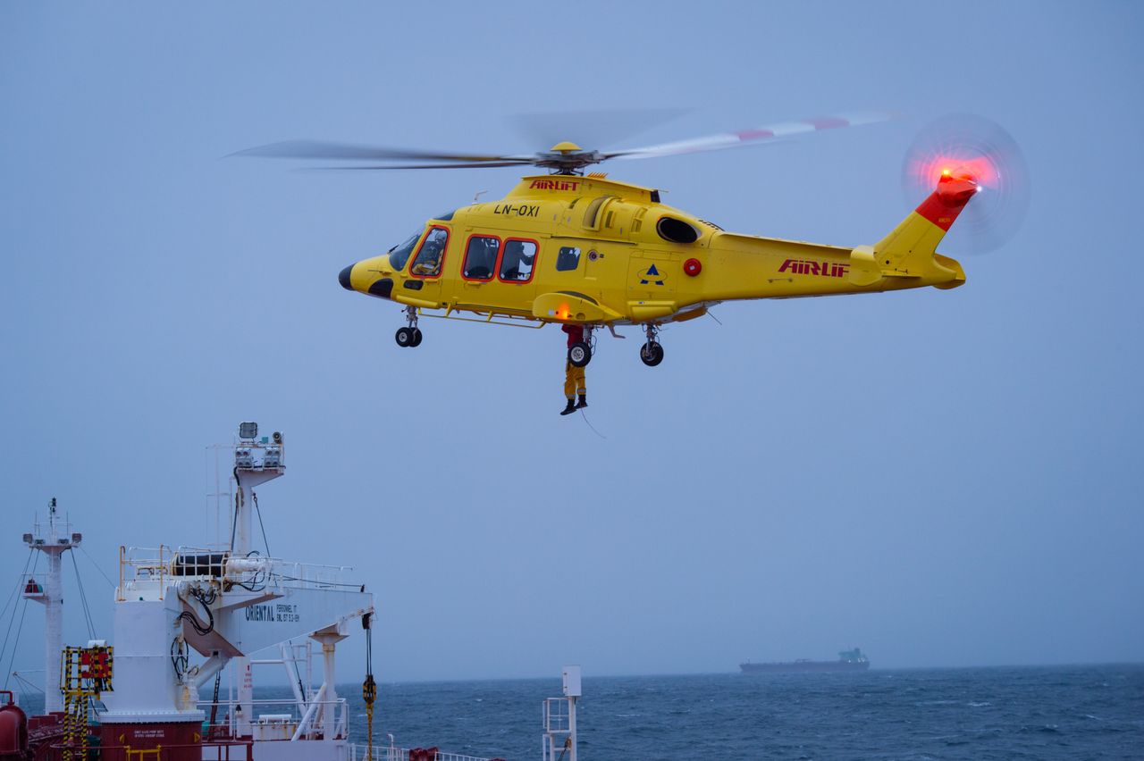 embark A yellow rescue helicopter hovers over a ship during an aerial operation over choppy waters.
